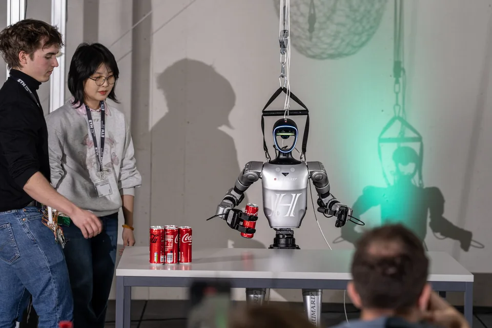 Two participants demonstrating a humanoid robot handling a drink can at the Hangar