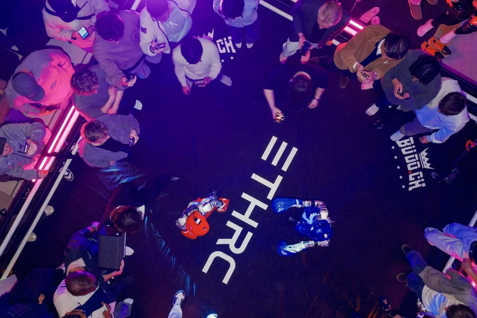 An overhead view of two robots in a boxing ring surrounded by the ETH Robotics Club community